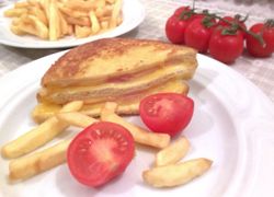 Sendvič plnený, v ňom šunka a syr, na tanieri aj hranolky a cherry paradajky, v pozadí tiež