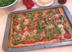 Plech s pizzou s paradajkovým základom, na vrchu paradajky, mozzarella a na upečenej pizzi čerstvá rukola