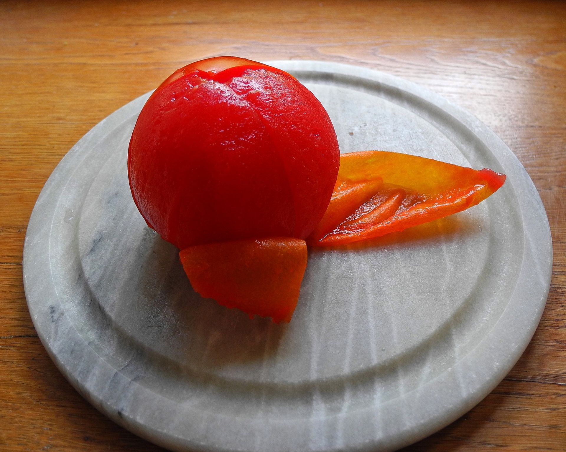 Trochu ošúpaná červená paradajka - začiatok šúpania na bielom tanieriku