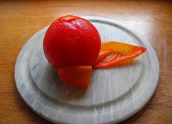 Trochu ošúpaná červená paradajka - začiatok šúpania na bielom tanieriku