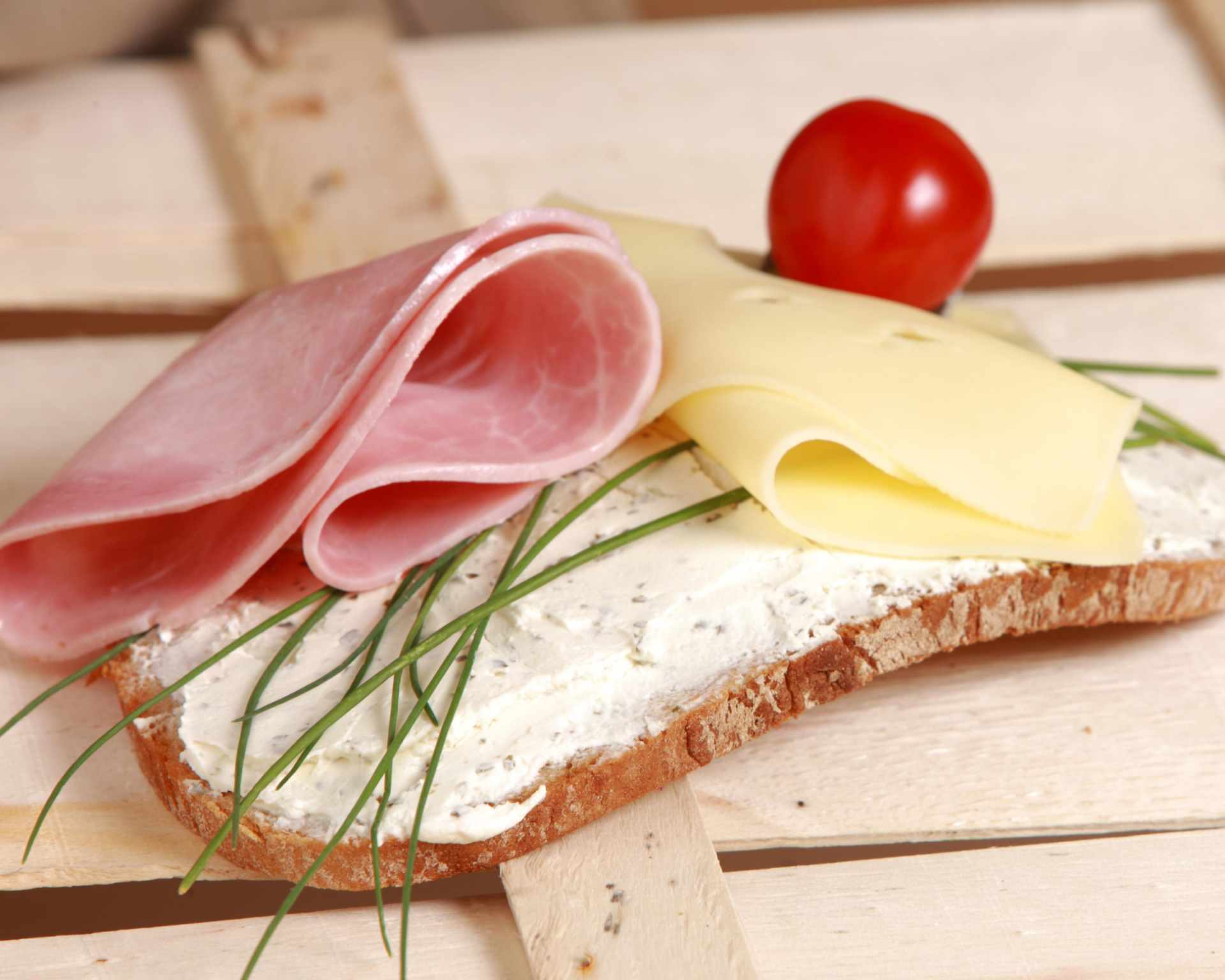 Plátky šunky, syra a pažítka na krajci chleba potretého pomazánkou. Ilustračné foto k priemyselnej výrobe šunky.