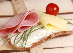 Plátky šunky, syra a pažítka na krajci chleba potretého pomazánkou. Ilustračné foto k priemyselnej výrobe šunky.