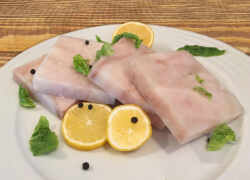 Surové rybie filé - kocky s nakrájanými plátkami citróna, celé čierne korenie a kúsky šalátu