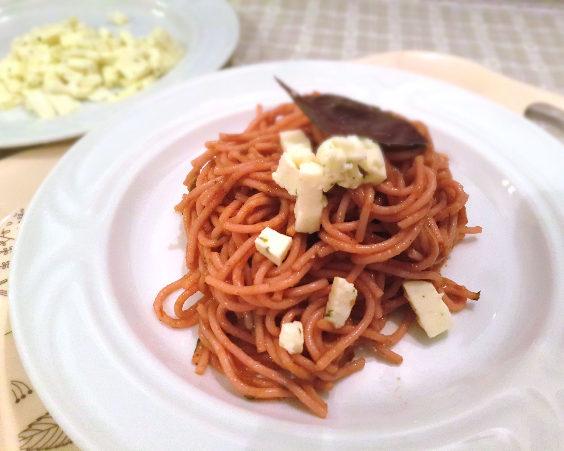 Krásne naservírované zakrútené paradajkové špagety so syrom na kocky ozdobené listom bazalky