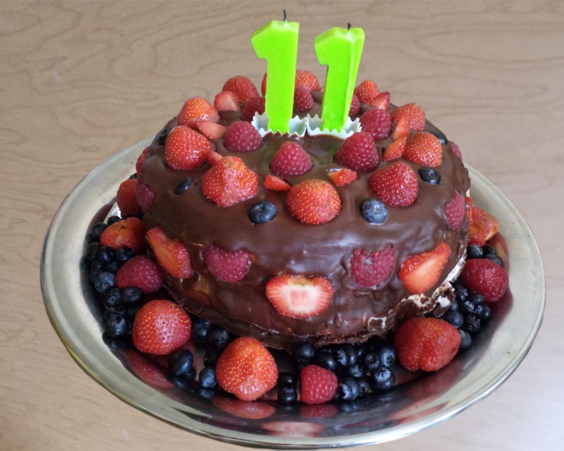Krásna čokoládovou polevou potretá torta plná jahôd, malín a čučoriedok so sviečkami na 11-te narodeniny