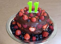 Krásna čokoládovou polevou potretá torta plná jahôd, malín a čučoriedok so sviečkami na 11-te narodeniny
