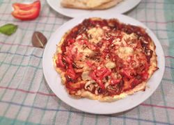 Krásny tenký slaný okrúhly pizza koláč s červenou paprikou, šampiňónmi a syrom na bielom okrúhlom tanieri