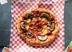 Pizza na červeno-bielej kockovanej servítke s hubami, salámou a paprikou