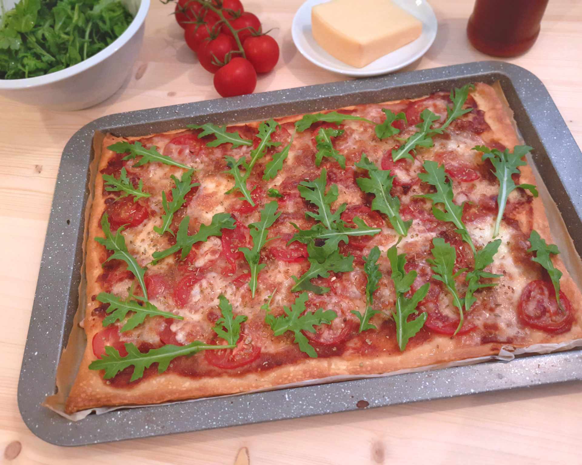 Plech s pizzou s paradajkovým základom, na vrchu paradajky, mozzarella a na upečenej pizzi čerstvá rukola