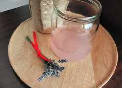 Nápoj z levandule v pohári, vedľa neho čerstvá levanduľa zviazaná červenou mašličkou