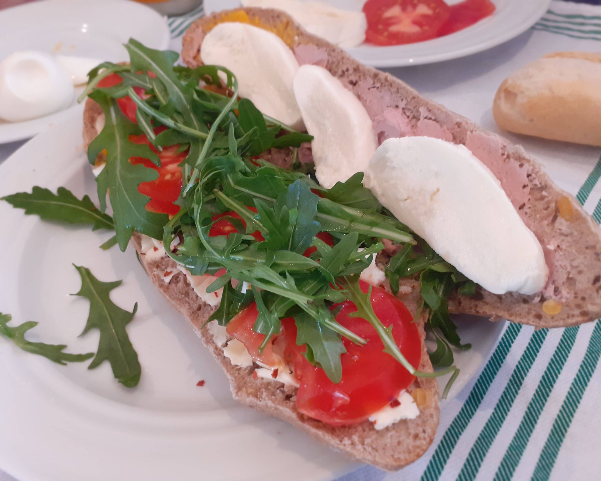 Bageta prekrojená, natretá paštikou a obložená mozzarellou paradajkami a rukolou.