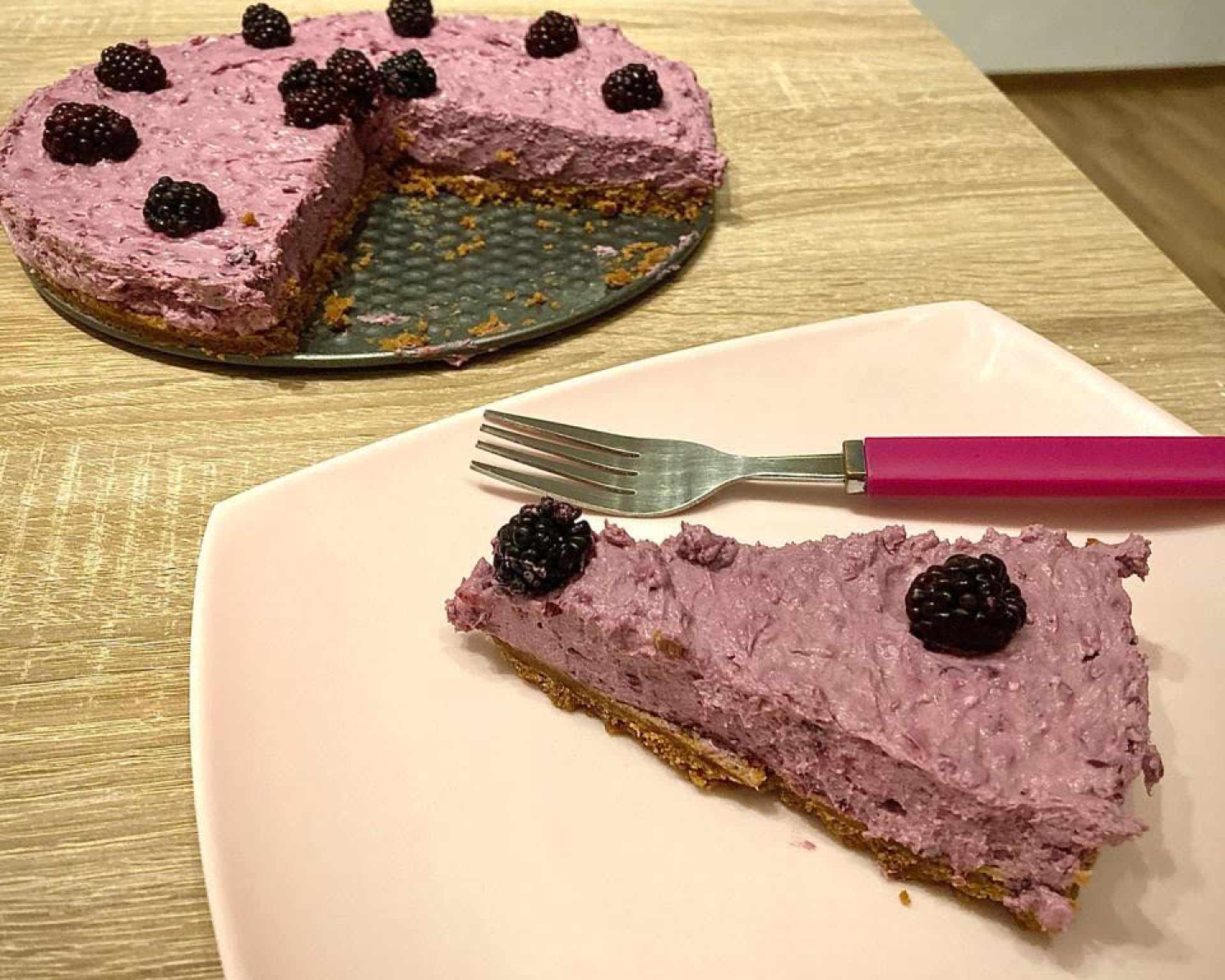 Hotový nepečený černicový cheesecake trojuholník na bielom hranatom tanieri s vidličkou