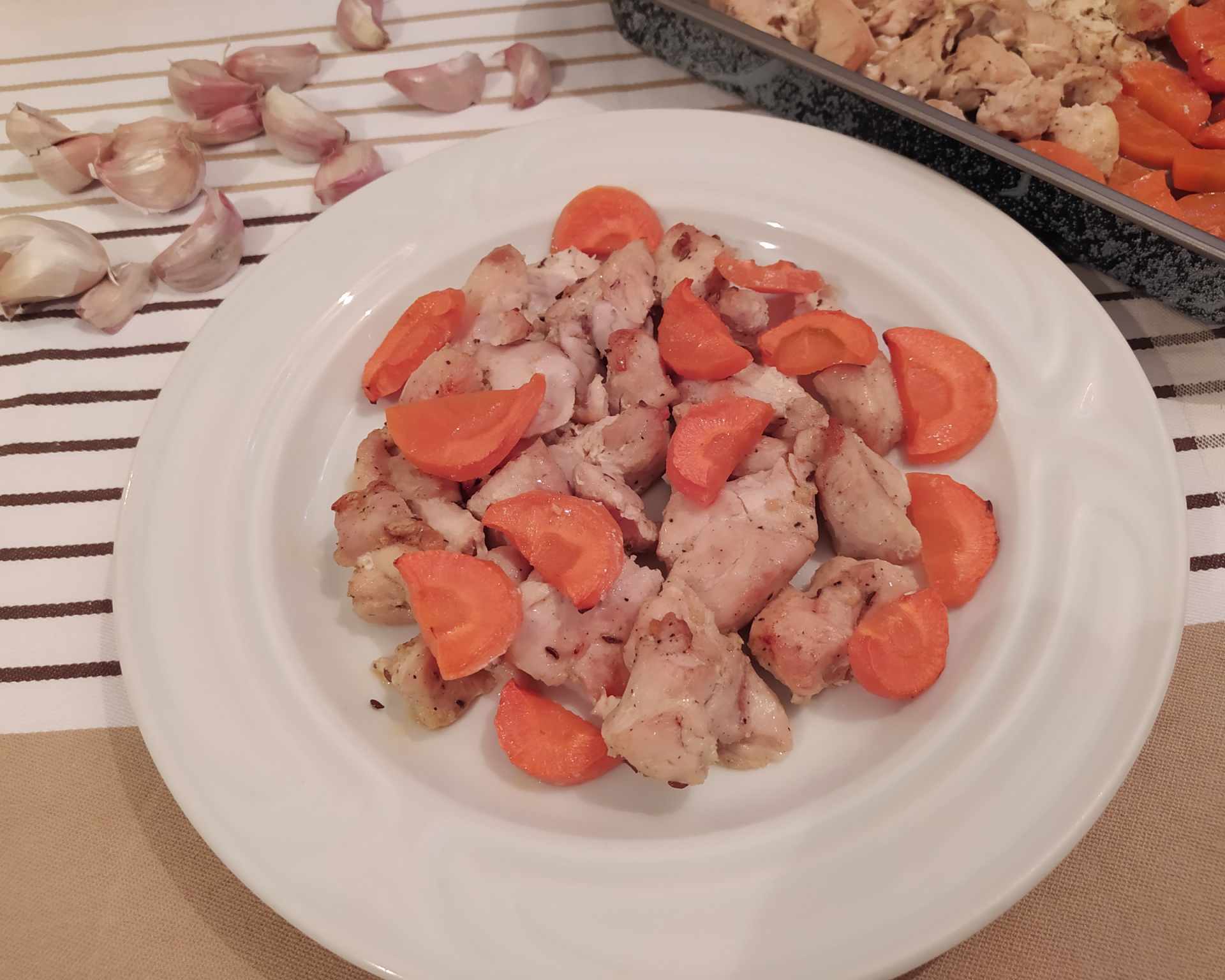 Upečené mäsko z kuraťa s krásne oranžovou upečenou mrkvou na bielom plytkom tanieri