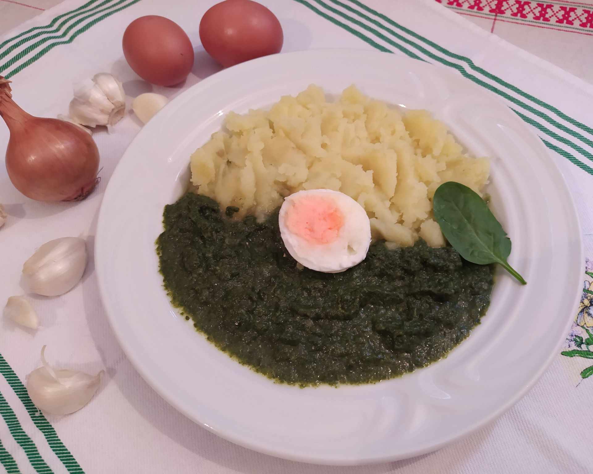Špenátový prívarok so zemiakovou kašou a vajíčkom na tvrdo na bielom tanieri