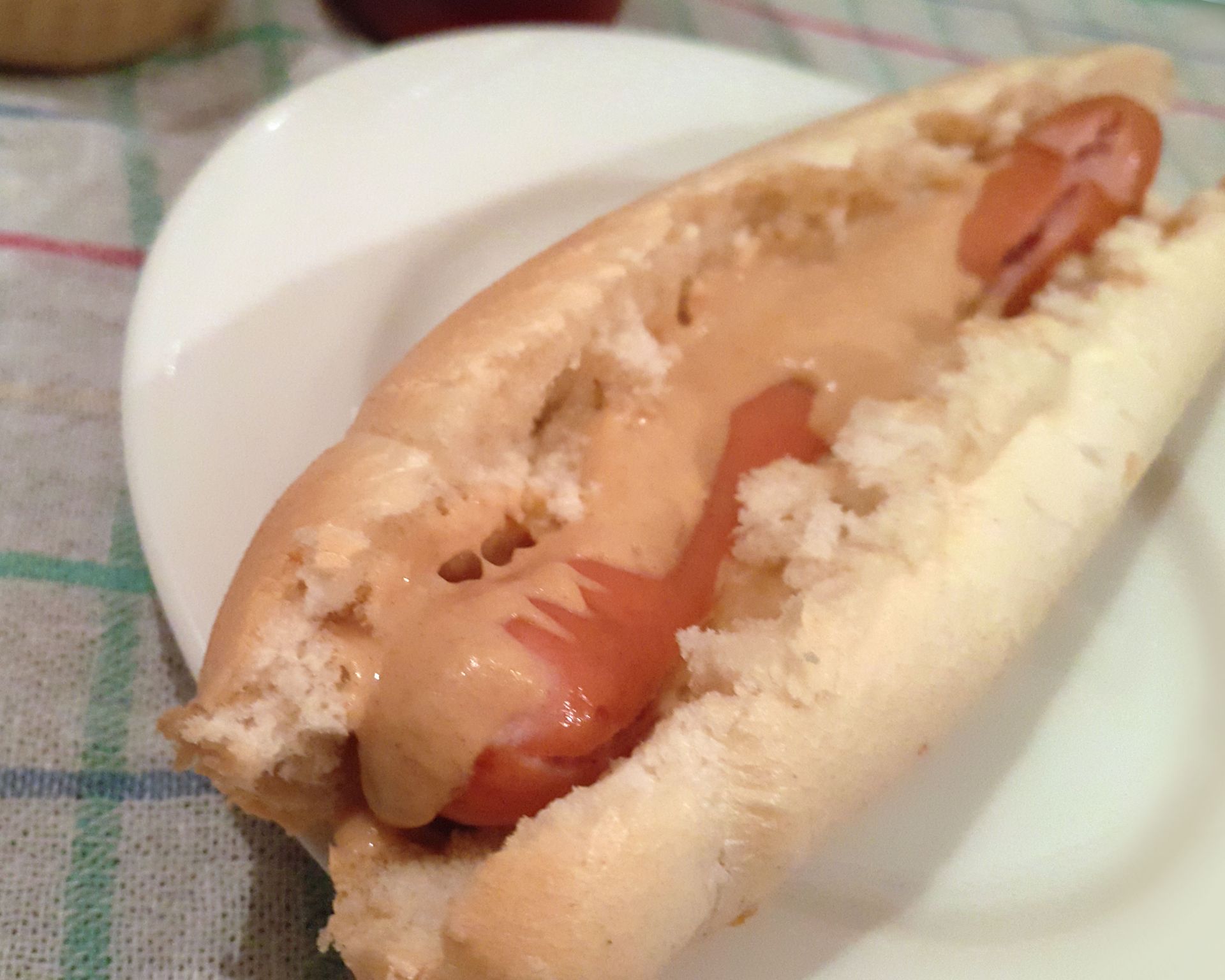 Párok v rozkrojenom rožku poliaty iba horčicou. Netypický americký hot-dog na bielom tanieri.