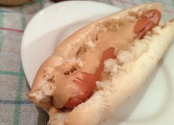 Párok v rozkrojenom rožku poliaty iba horčicou. Netypický americký hot-dog na bielom tanieri.