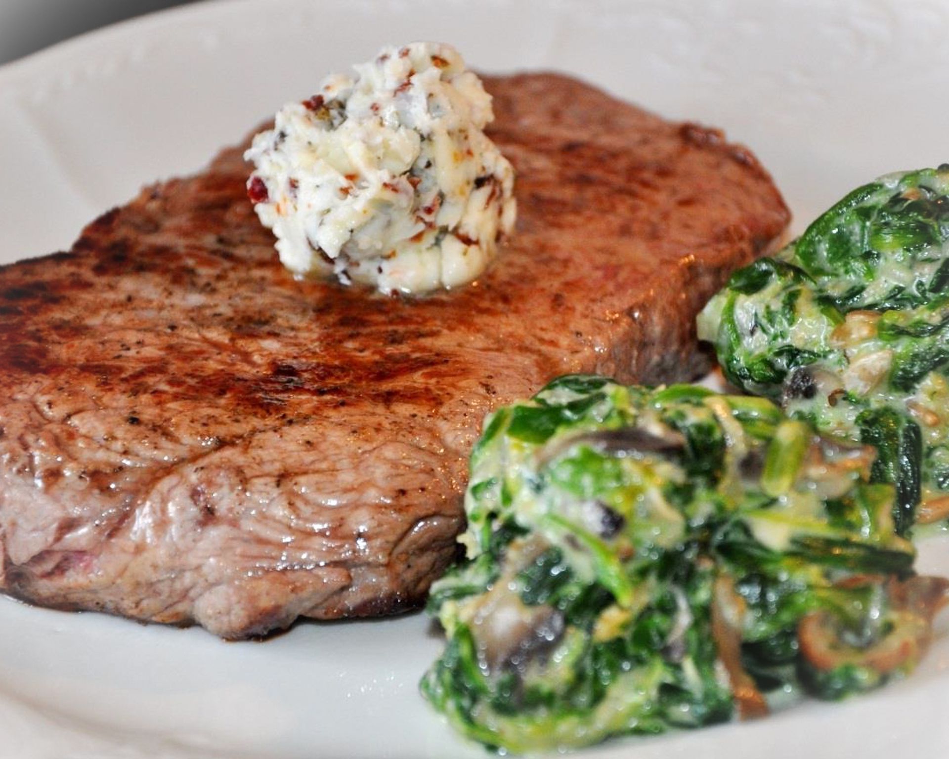 Steak z hovädzeho mäsa na tanieri so špenátom. Na vrchu je ozdobený kopčekom bylinkového masla.