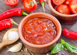 Červená salsa omáčka v miske, okolo štipľavé papričky