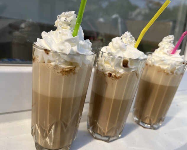 Hotová vietnamská ľadová káva so šľahačkou v sklenených vysokých pohároch so slamkou