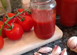 Paradajkový kečup s civklou v sklenenom pohári na doske, cesnak a paradajky
