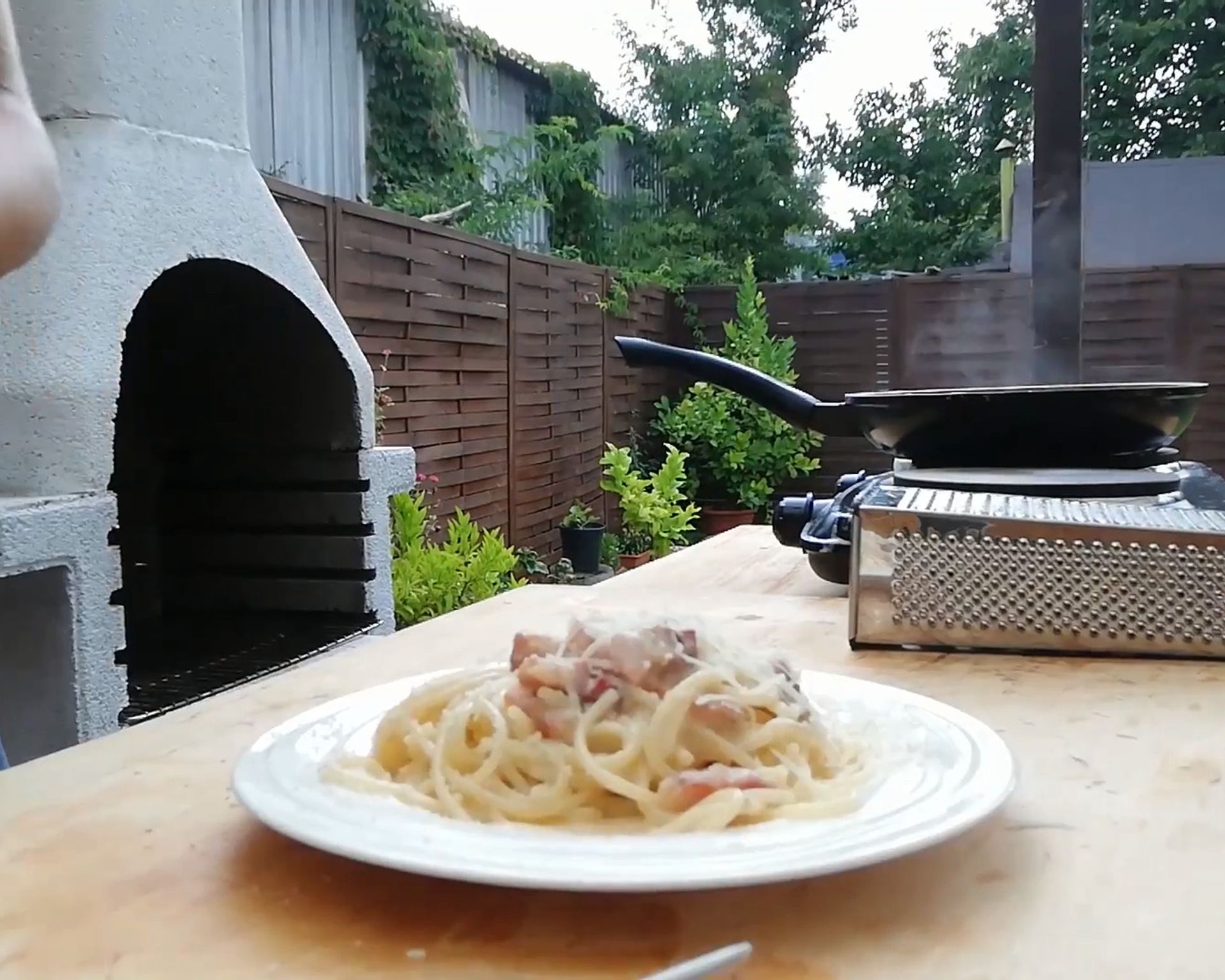 Špagety carbonara na tanieri, na stole, v pozadí strúhadlo a panvica