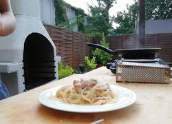 Špagety carbonara na tanieri, na stole, v pozadí strúhadlo a panvica