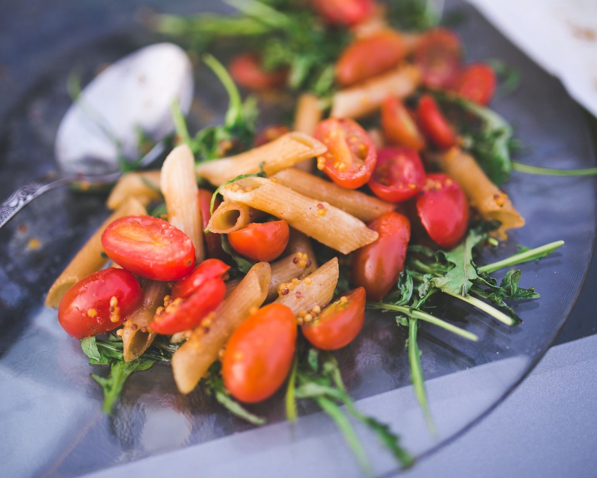 Penne s cherry paradajkami, čerstvá rukola a konopné semienka na sklenenom tanieri