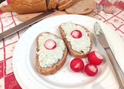 Dva chlebíky s nátierkou z Nivy s reďkovkami na tanieri s nožíkom