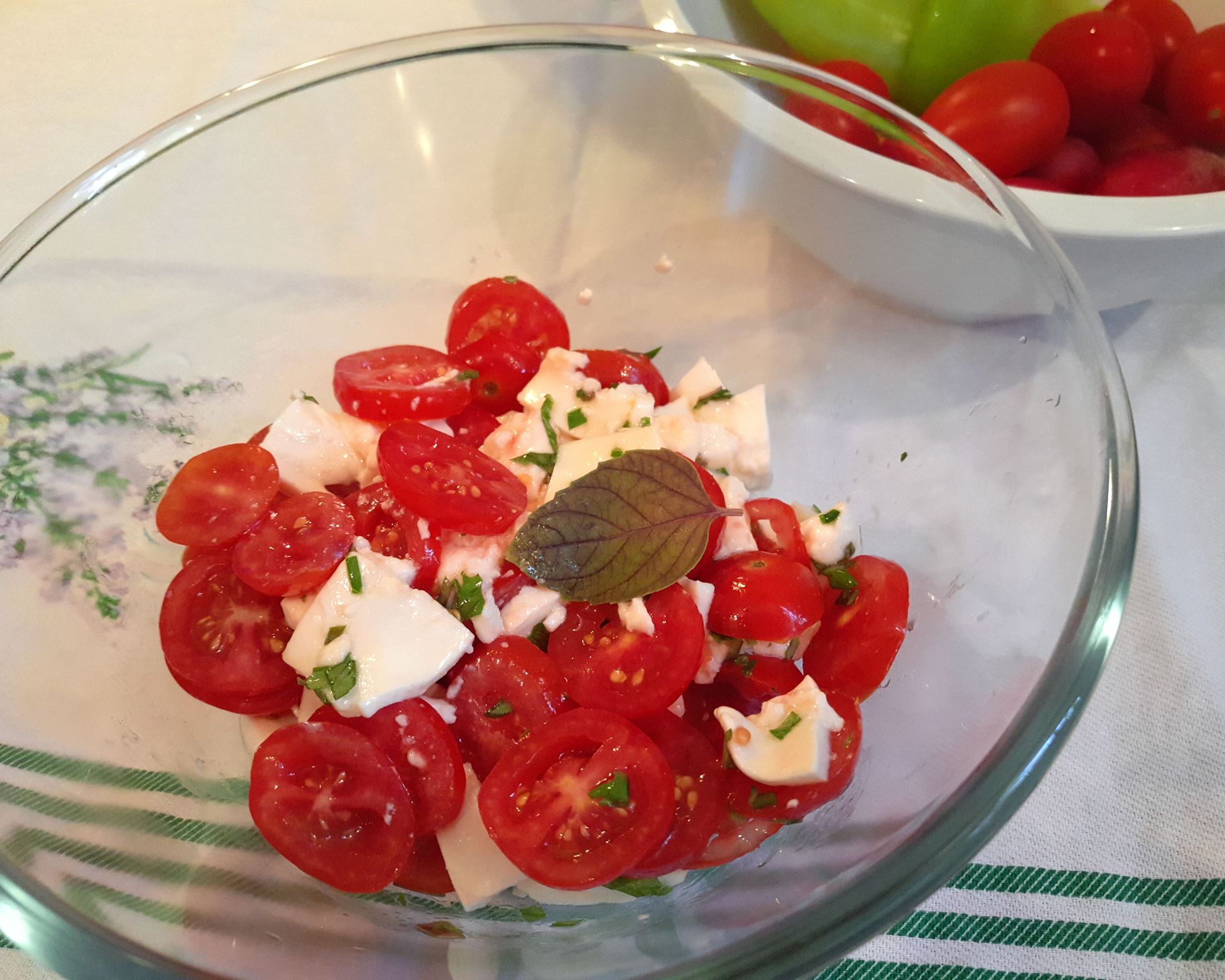 Šalát z paradajok a mozzarelly v sklenenej miske s ozdobným lístkom bazalky