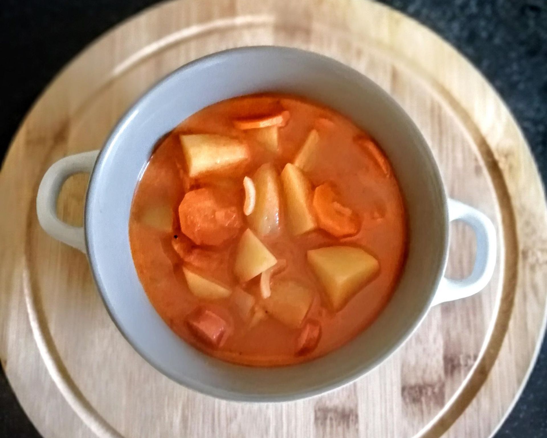 Gulášová polievka so zemiakmi a párky v hrnčeku s uškami na drevenej tácke, ostrá polievka