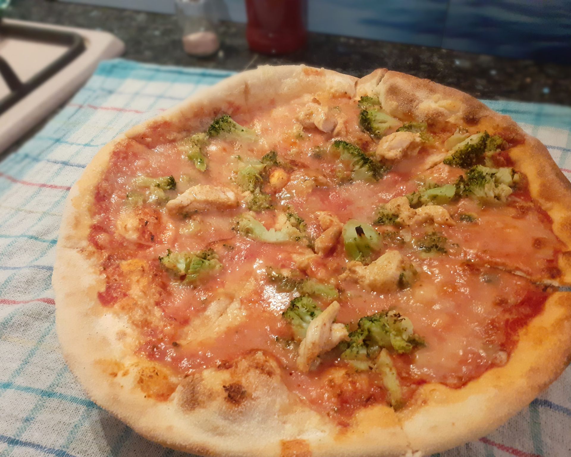 Doma pečená okrúhla pizza z klasického cesta ozdobená kuraťom a šunkou, brokolica