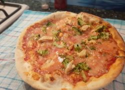 Doma pečená okrúhla pizza z klasického cesta ozdobená kuraťom a šunkou, brokolica
