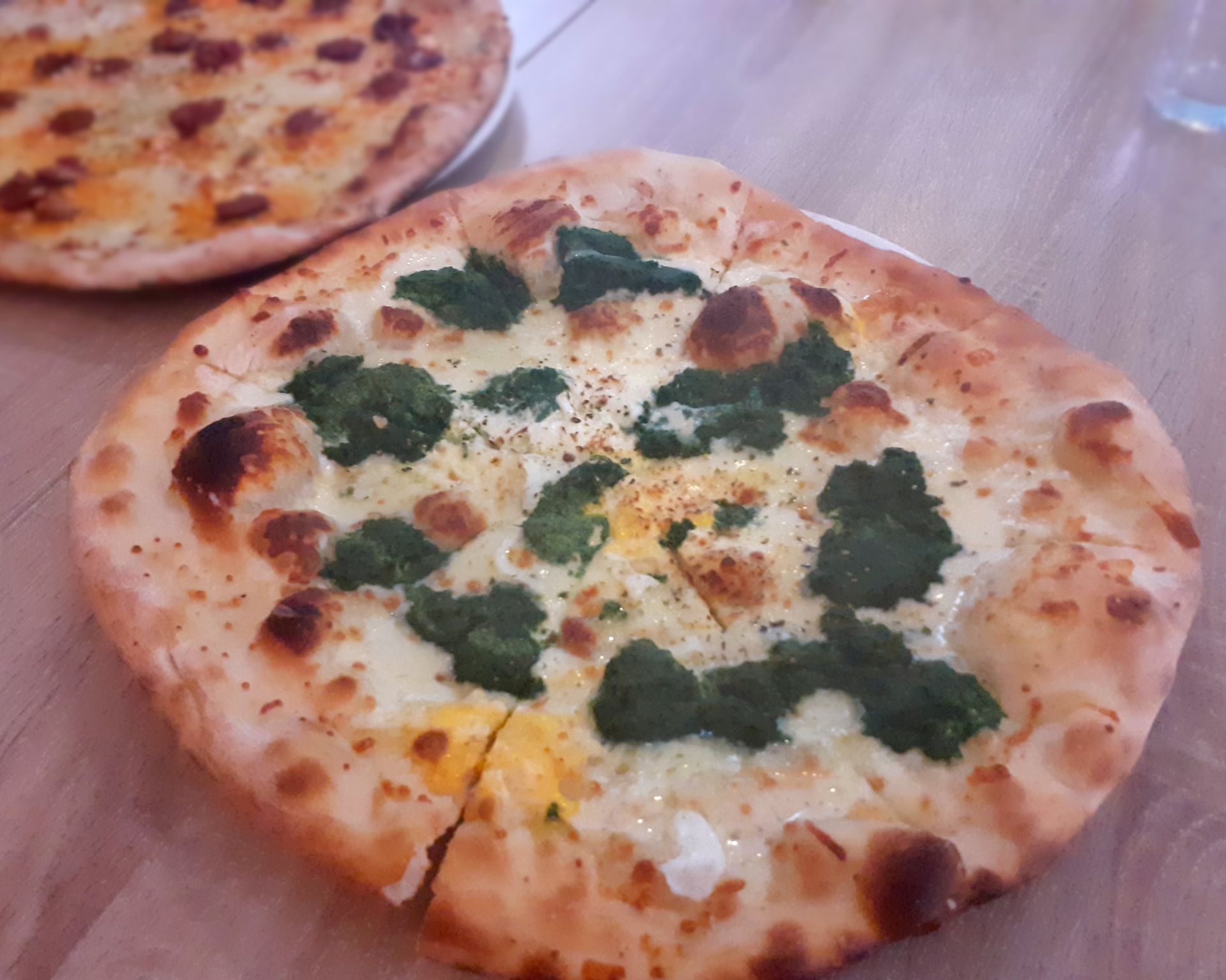 Pizza so smotanovým základom, špenátom, syrom a vajcom, v pozadí klobásová pizza
