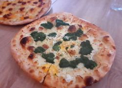 Pizza so smotanovým základom, špenátom, syrom a vajcom, v pozadí klobásová pizza