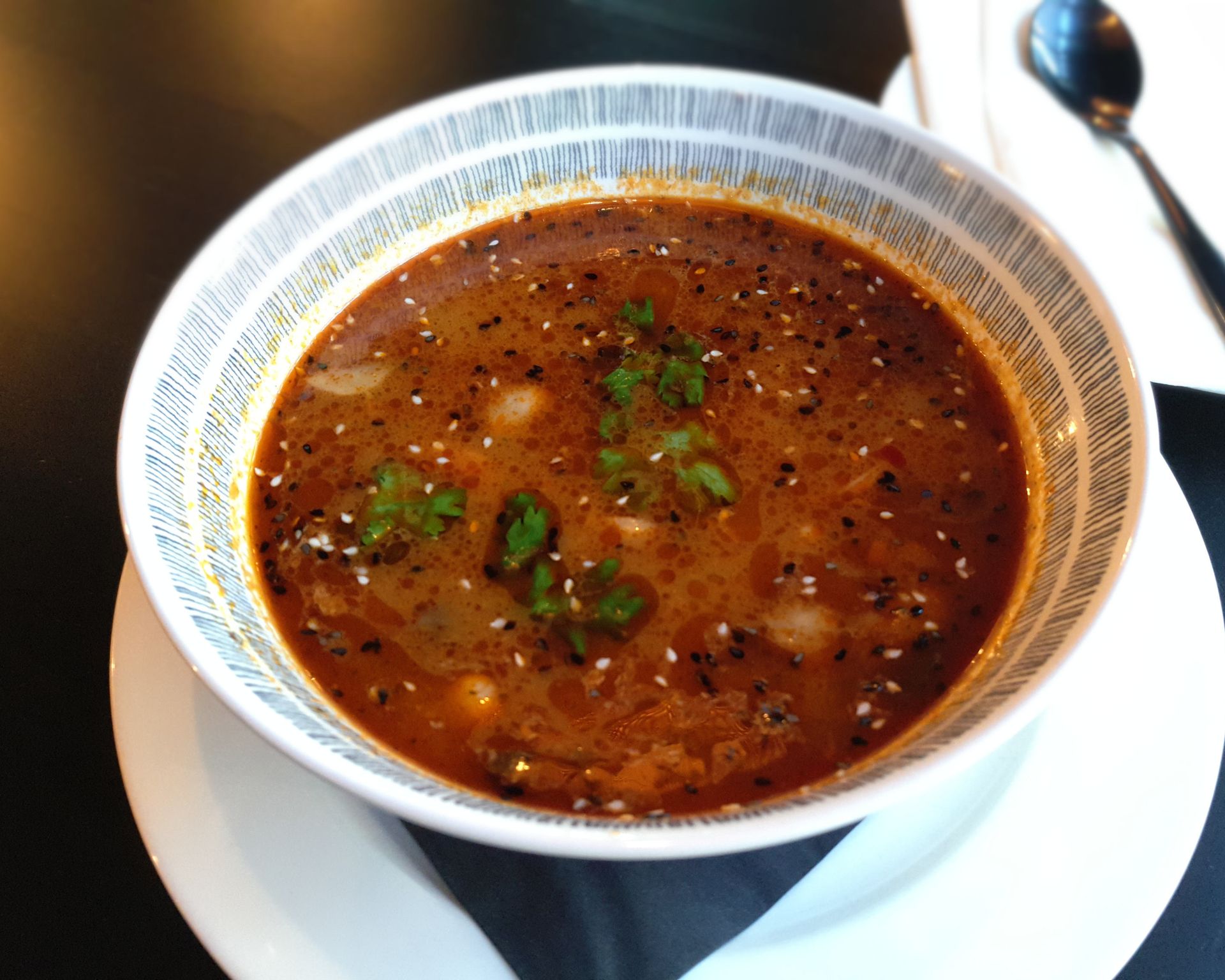 Hotová polievka Tom Yum vo veľkej miske ozdobená koriandrom a sezamom