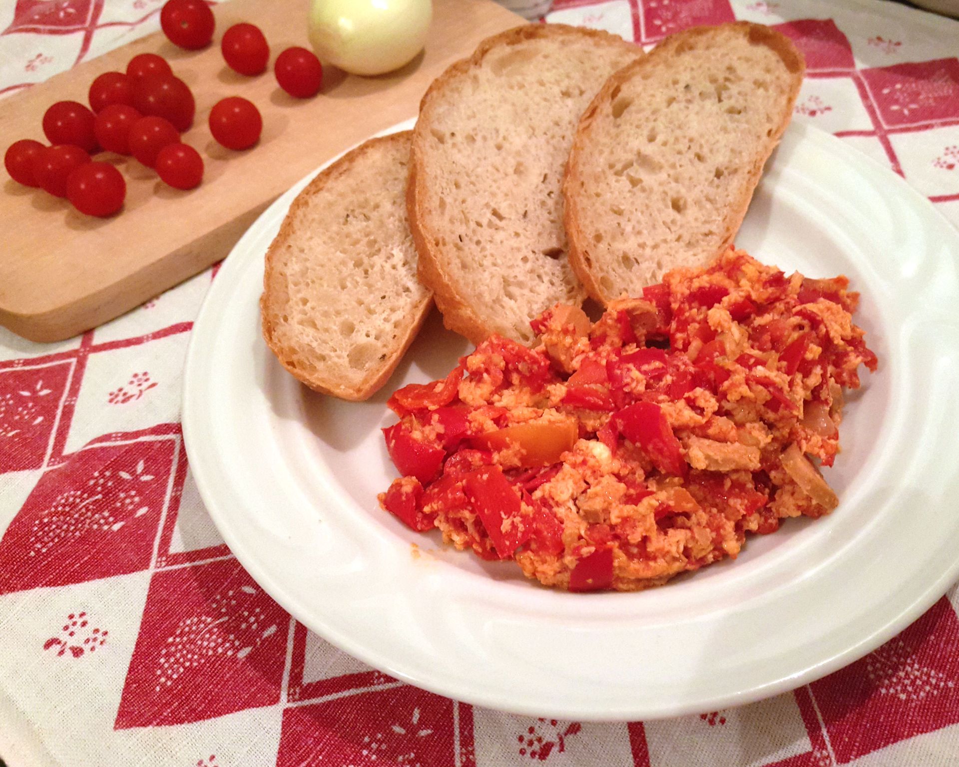 Vajcové lečo s červenou paprikou s krajcami chleba, v pozadí cherry paradajky a cibuľa