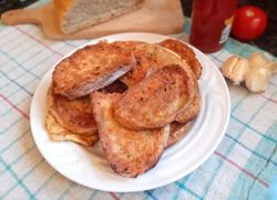 Suchý opečený chlebík vo vajci na bielom tanieri. V pozadí chlieb, kečup, paradajka a cesnak. Vajcový chlieb