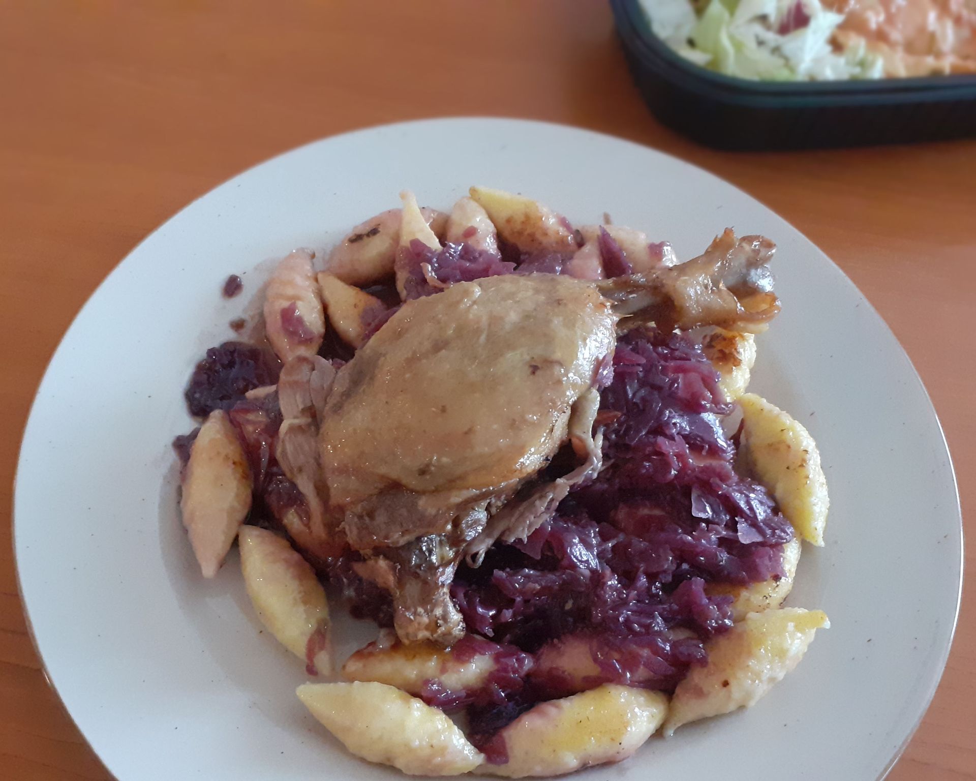 Upečené šťavnaté kačacie stehná z kačky na červenej kapuste, dookola zemiakové haluštičky na bielom tanieri