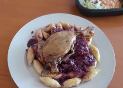 Upečené šťavnaté kačacie stehná z kačky na červenej kapuste, dookola zemiakové haluštičky na bielom tanieri