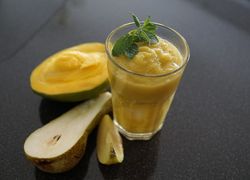 Nápoj v priesvitnom pohári, prekrojené mango a hruška