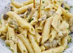 Penne s kuracím mäsom v smotanovej omáčke. Cestoviny sú posypané bazalkou.