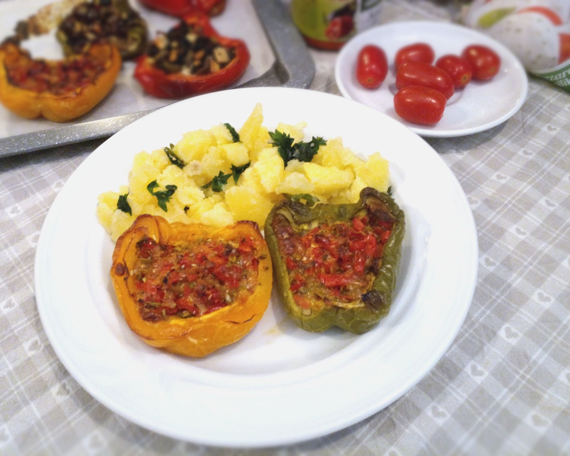 Žltá a zelená opekaná paprika plnená paradajkami a mozzarellou s varenými zemiakmi na bielom tanieri