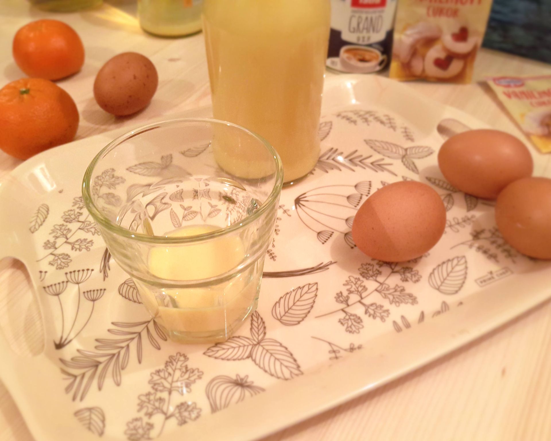 Vajcový likér v pohári, v pozadí fľaška plná likéru, vajíčka na tácke
