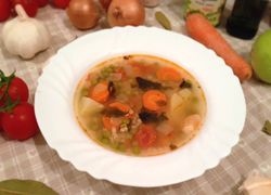 Mrkvová polievka s hráškom, paradajkami a jačmennými krúpmi v peknom bielom ozdobnom tanieri, okolo veľa čerstvej zeleniny