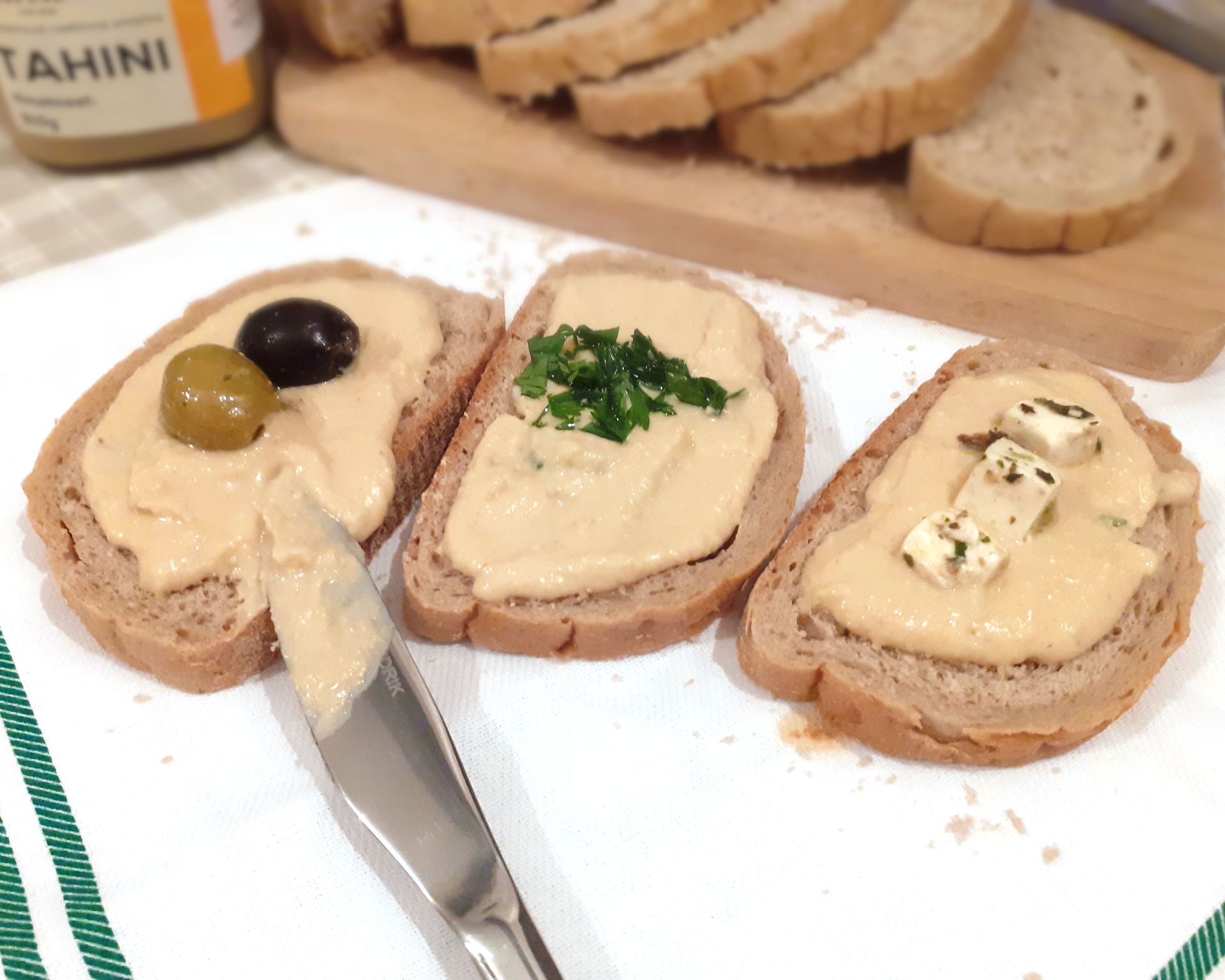 Tri krajce chlebíka natreté domácim humusom. Ozdobené olivami, feta syrom a petržlenovou vňaťou.