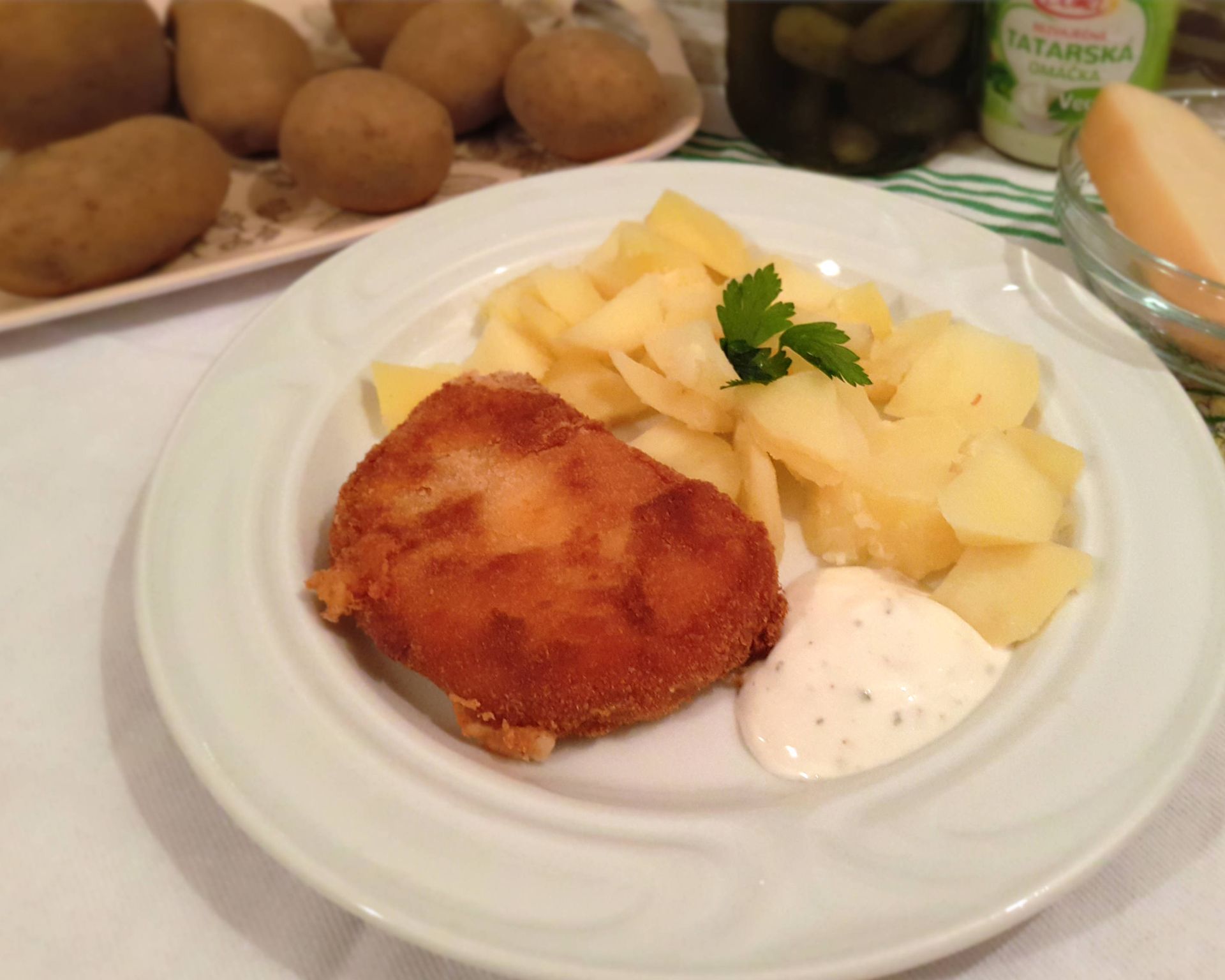 Tvrdý syr v trojobale s varenými zemiakmi, na nich petržlenová vňať, vedľa tatárska omáčka