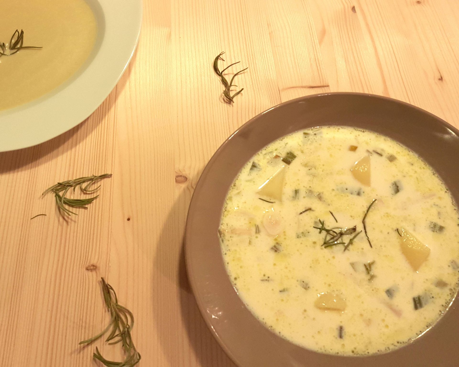 Mliečna polievka zo surovín podľa receptu. Nabratá je v tmavej miske a na drevenom stole. Výrazné sú zemiaky a rozmarín.