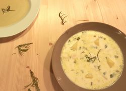 Mliečna polievka zo surovín podľa receptu. Nabratá je v tmavej miske a na drevenom stole. Výrazné sú zemiaky a rozmarín.