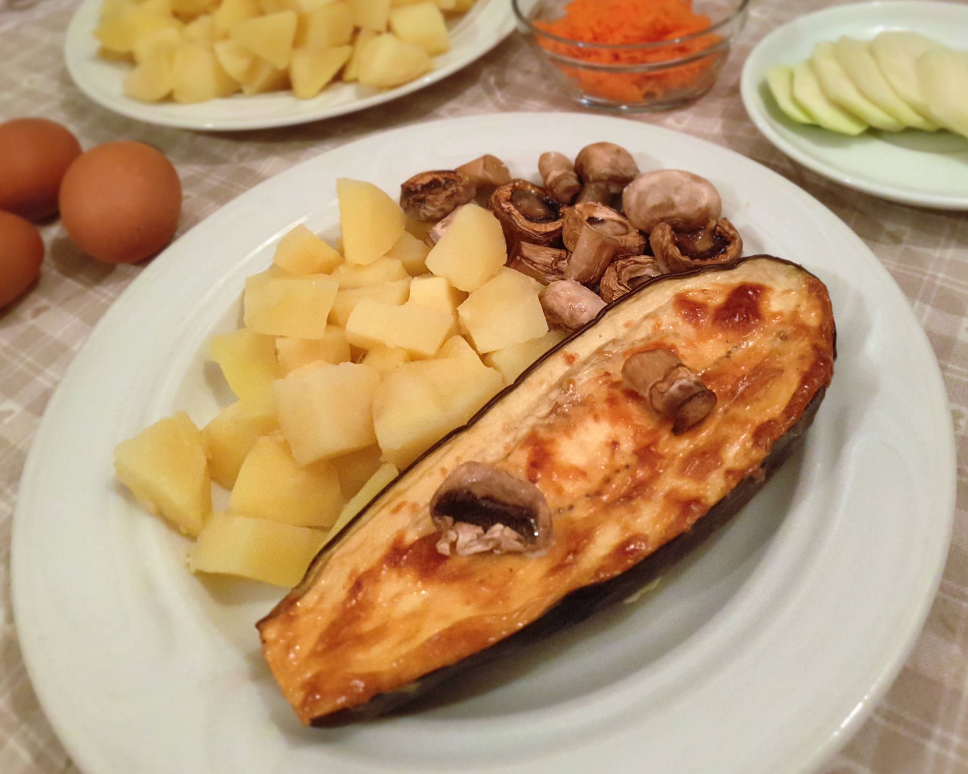 Polovica prekrojeného baklažánu upečená, plnená šampiňónmi s varenými zemiakmi a opečenými hubami