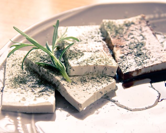 Plátky tofu na tanieri, podliate sójovou omáčkou a posypané bylinkami